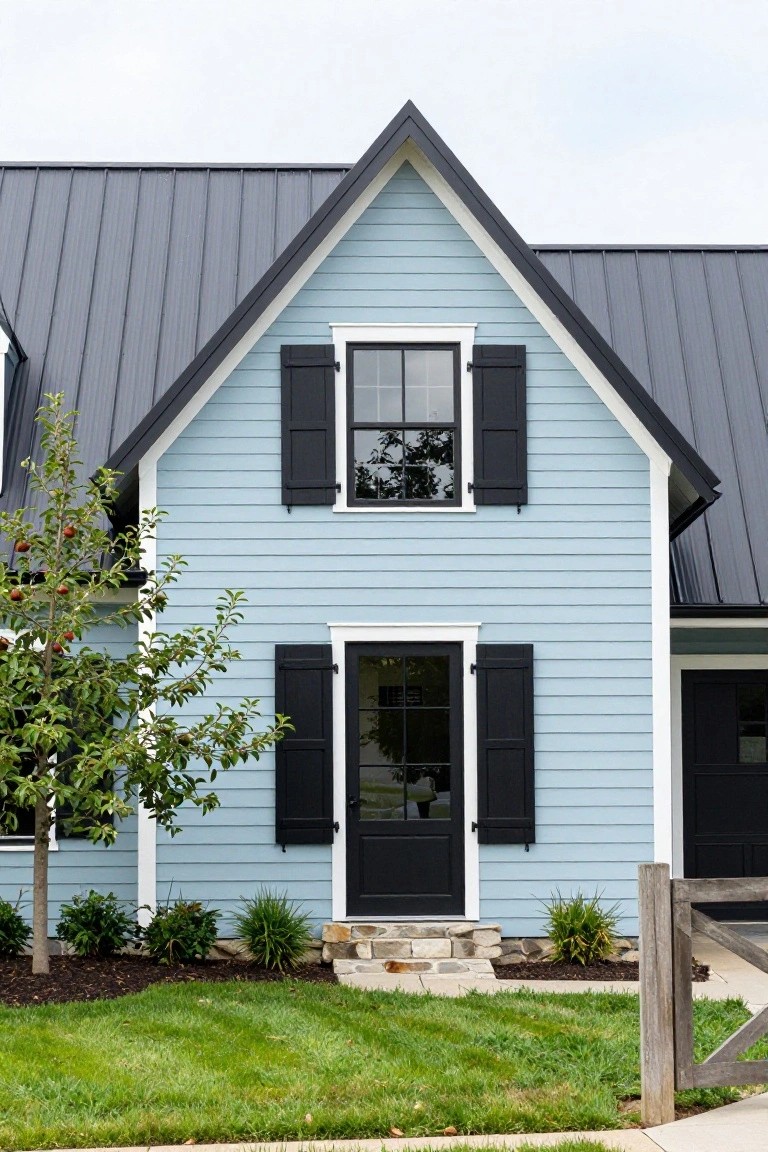 Light blue clapboard-sided gable house with dark metal roof, black shutters on white-framed windows, black front door with stone steps, apple tree and landscaping in front yard.