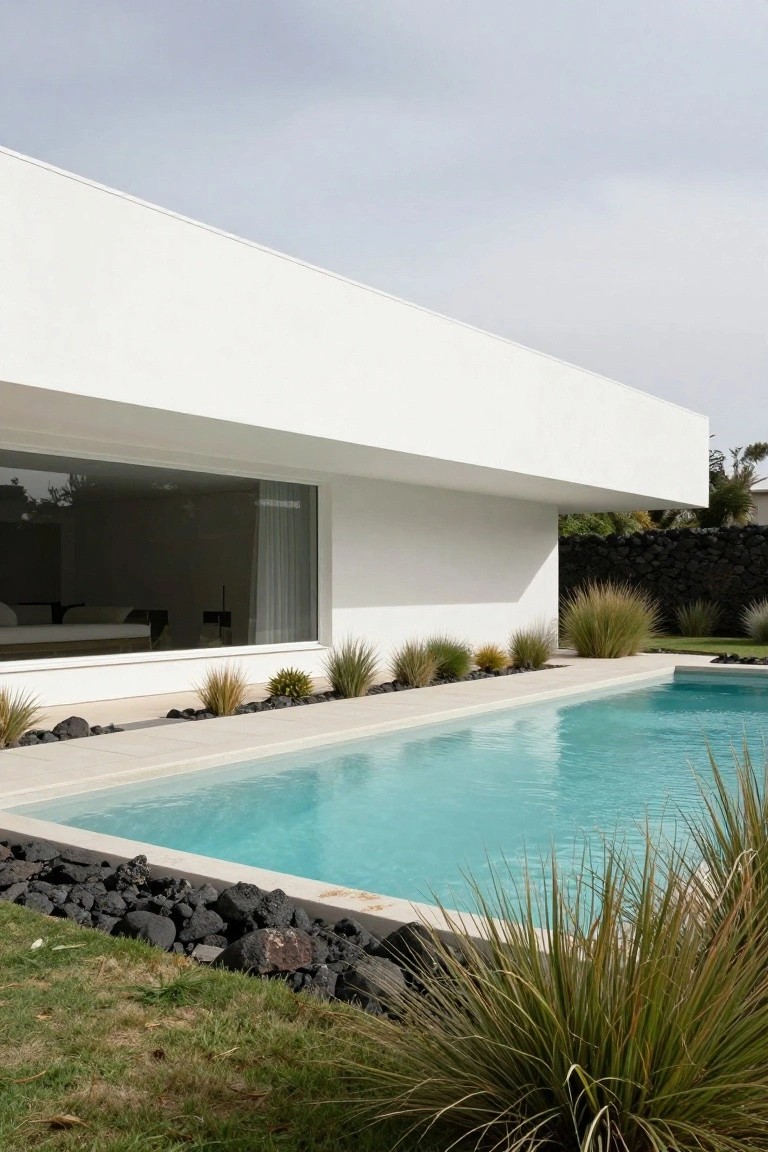 Modern white villa with turquoise pool, black lava rocks, and tall grasses.