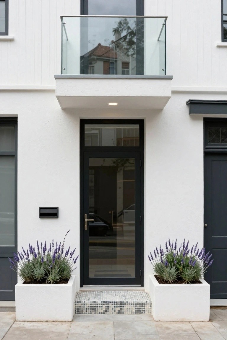 White house entrance with black door, lavender planters, mosaic step, and glass balcony above.
