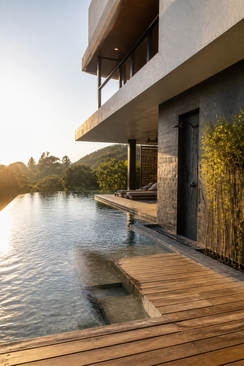 A modern concrete house with a large cantilevered upper floor extending over an infinity pool and wooden deck surrounded by greenery.