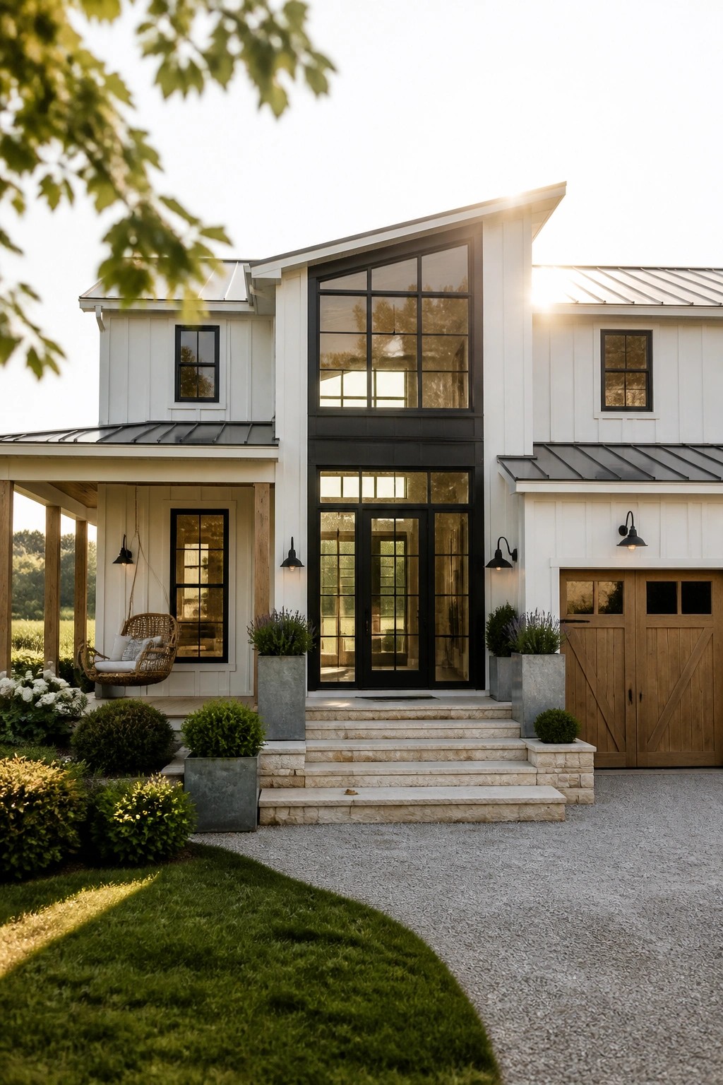 A modern two-story white house with black-framed windows and a tall central glass entry above double doors, a covered porch with a hanging chair, and a wooden garage on the right.