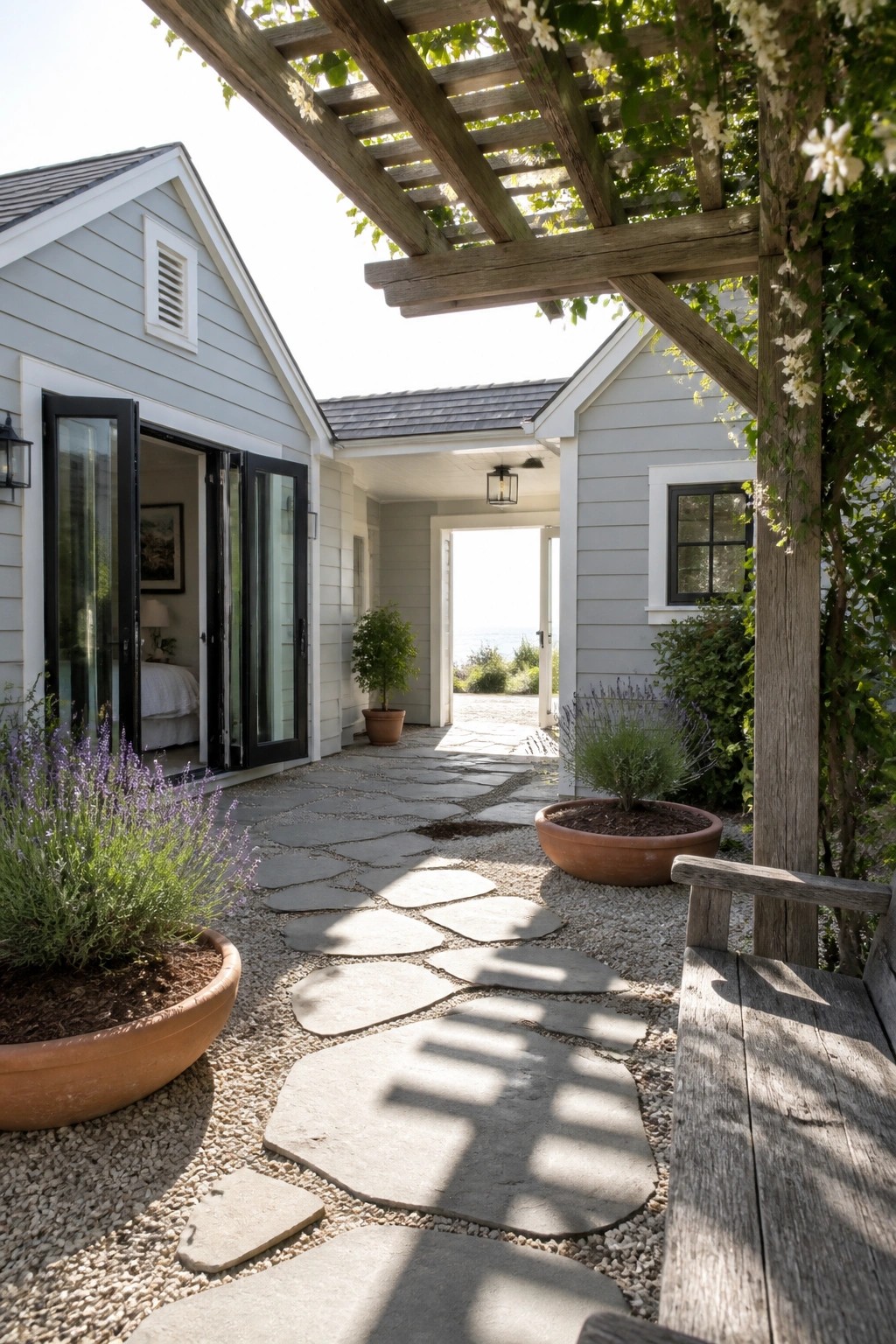 Stone pathway through shaded courtyard between cottages with ocean view beyond.