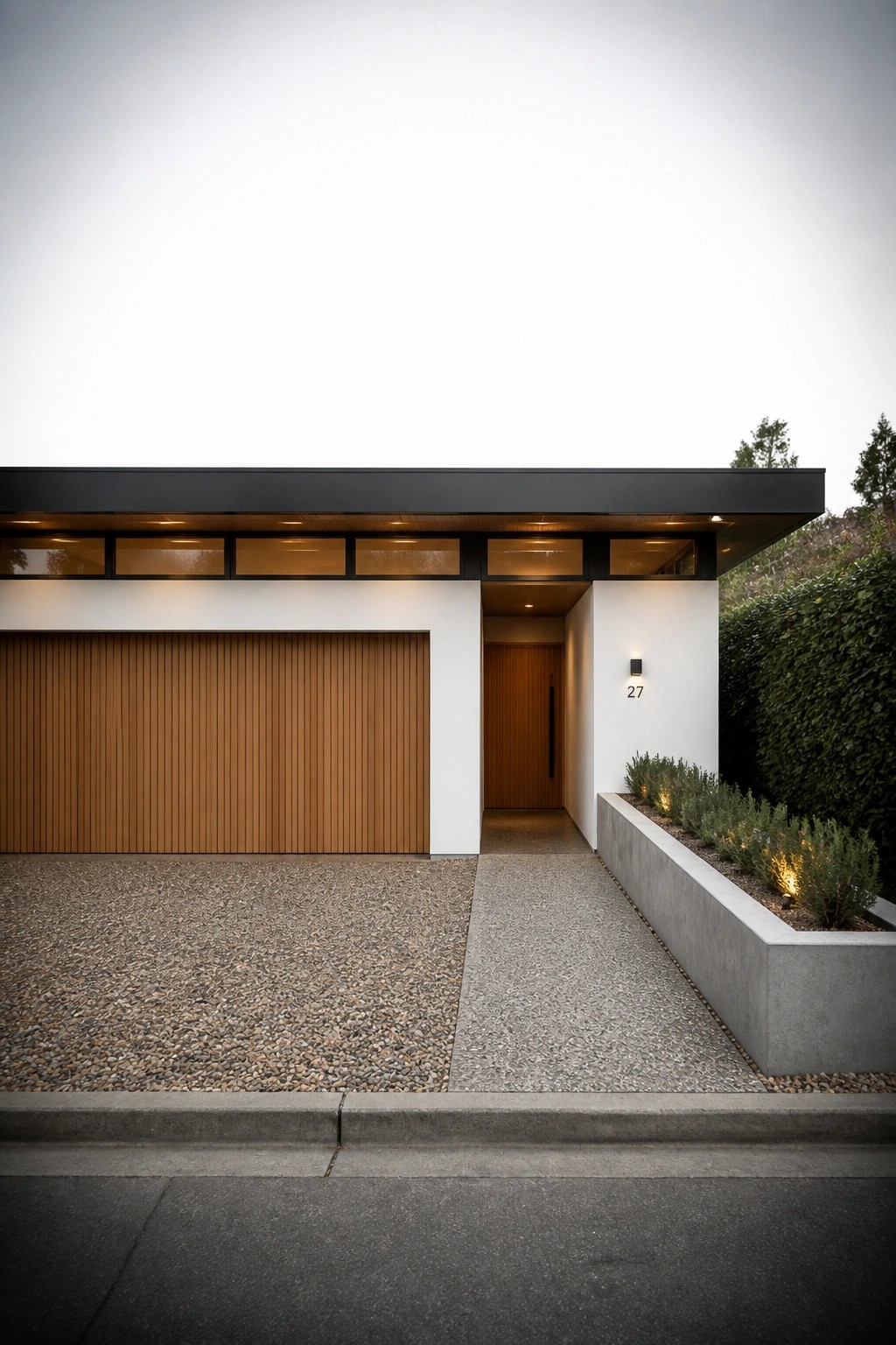 A modern single-story house with a flat black roof, wooden garage door, white walls, and a covered entry walkway next to a concrete planter bed.