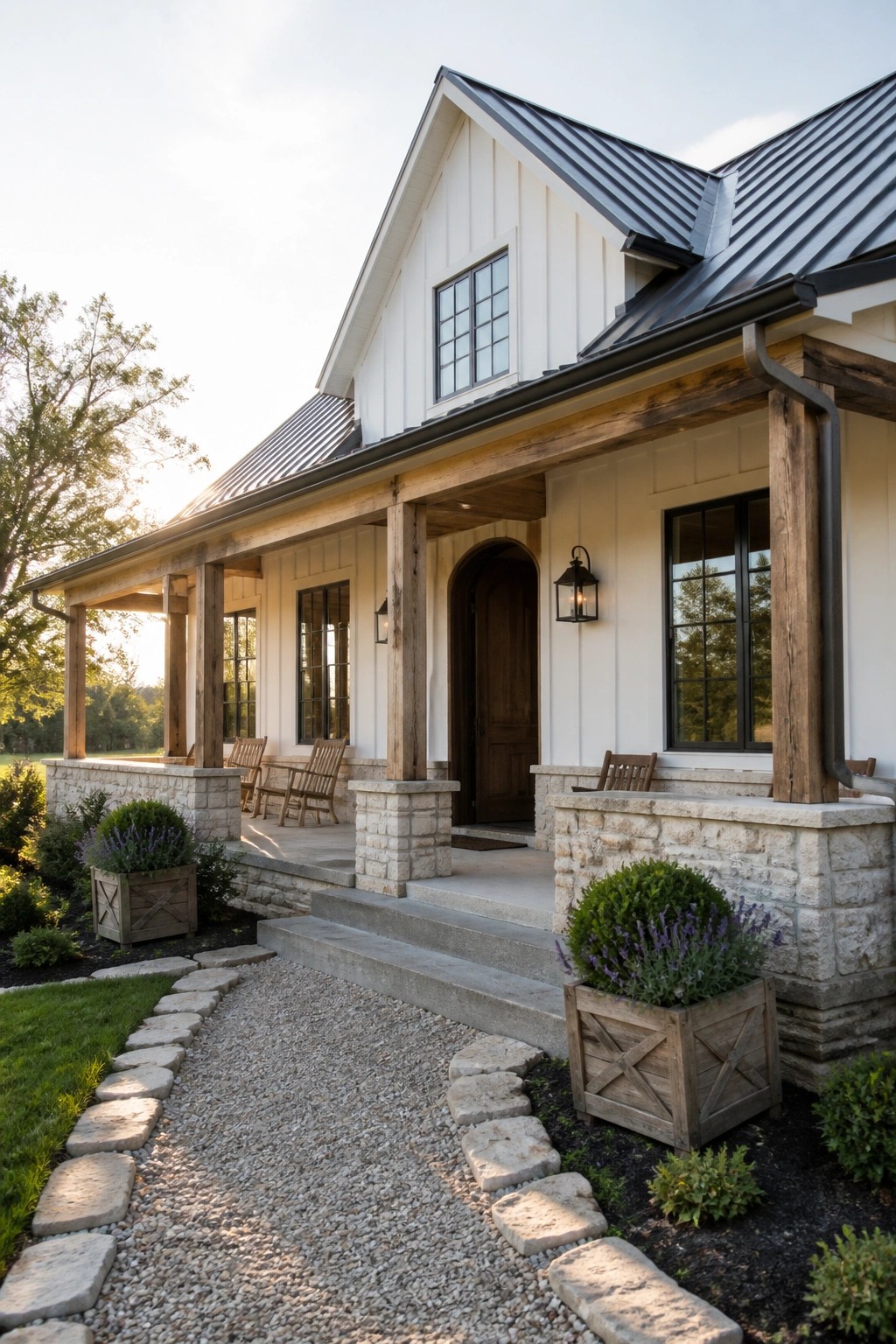 Modern farmhouse exterior featuring white board and batten siding, a dark standing seam metal roof, wooden porch posts on stone piers, and a central arched entry door.