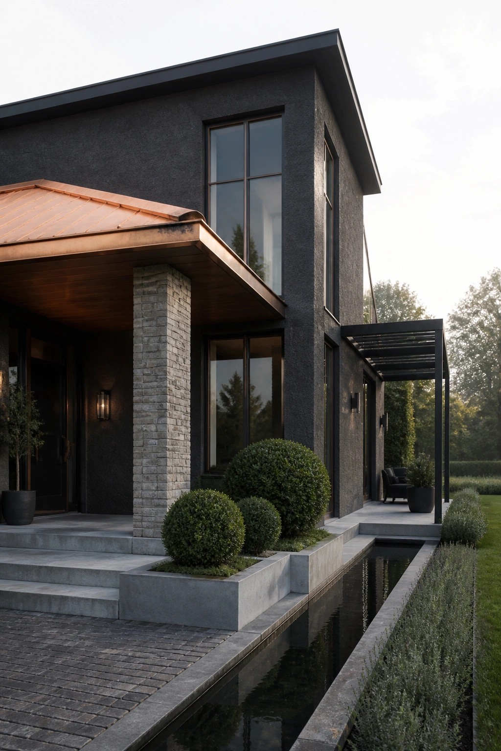 Modern dark gray house with copper roof overhang, stone pillar, and long rectangular water channel running parallel to the front facade.