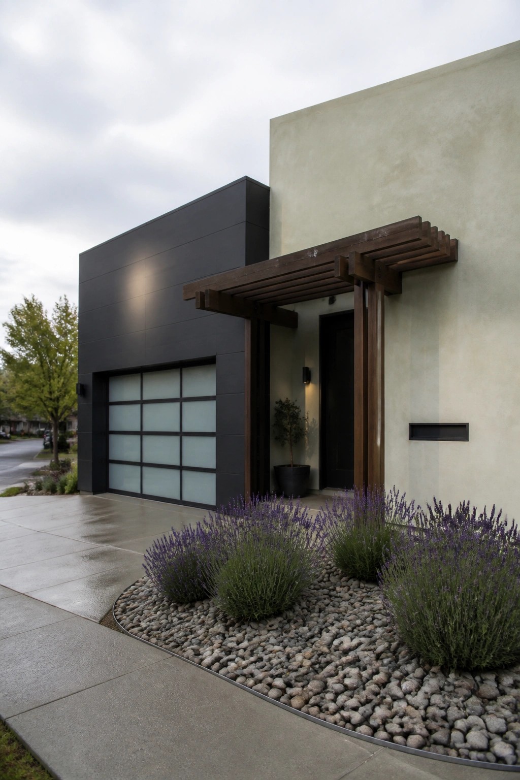 Modern house exterior with black paneling on the left, light stucco on the right, a dark garage door, and a wooden pergola structure over the front entrance with lavender plants in gravel beds.