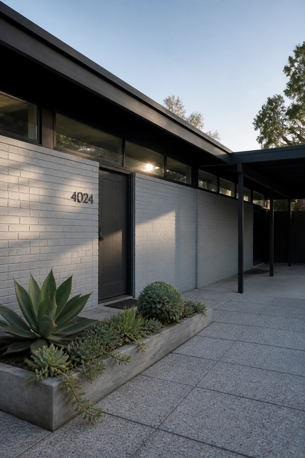 A modern single-story house exterior featuring white painted brick walls, a black door with the number 4024, black window frames, and a concrete planter with succulents along the front.