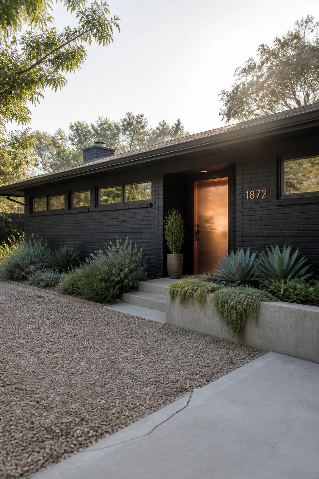 A modern single-story black brick house with a copper door, concrete steps, and gravel driveway in front.
