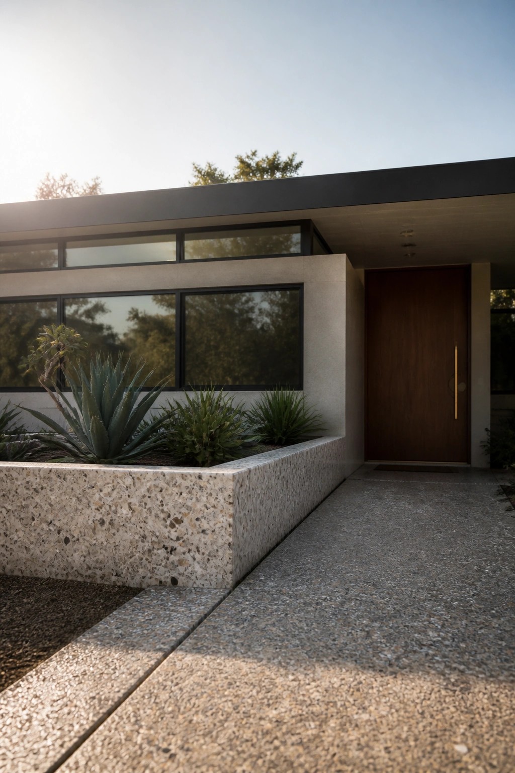 Modern house entrance with a large raised speckled concrete planter holding succulents beside a wooden door and tall windows.
