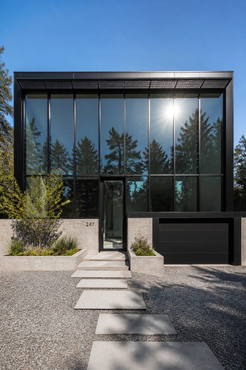 Modern two-story house with a full-width black-framed glass facade, central glass door, concrete planters and steps, and a gravel path with concrete pavers leading to the entrance.
