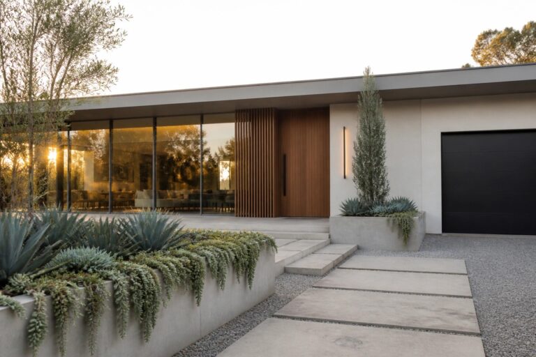 Modern house with concrete planters, agave plants, wooden door, and stone steps at dusk.