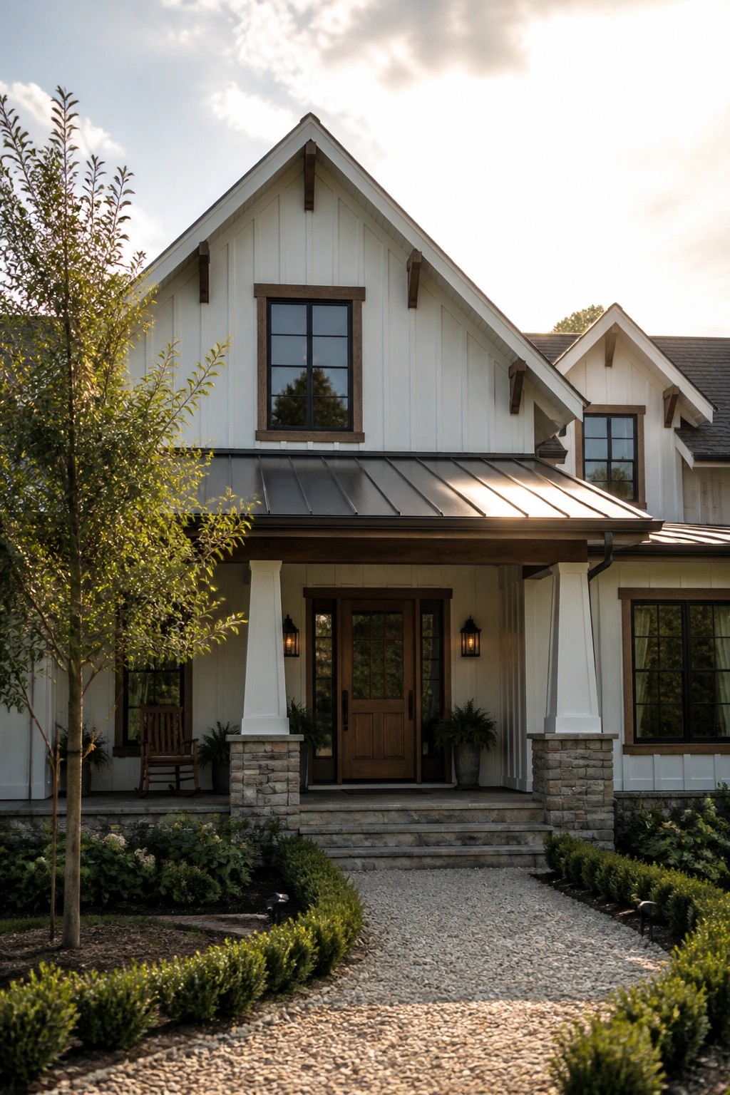A white house with a steep gable roof in dark metal, wood trim accents, and a covered front porch supported by white columns on stone bases.