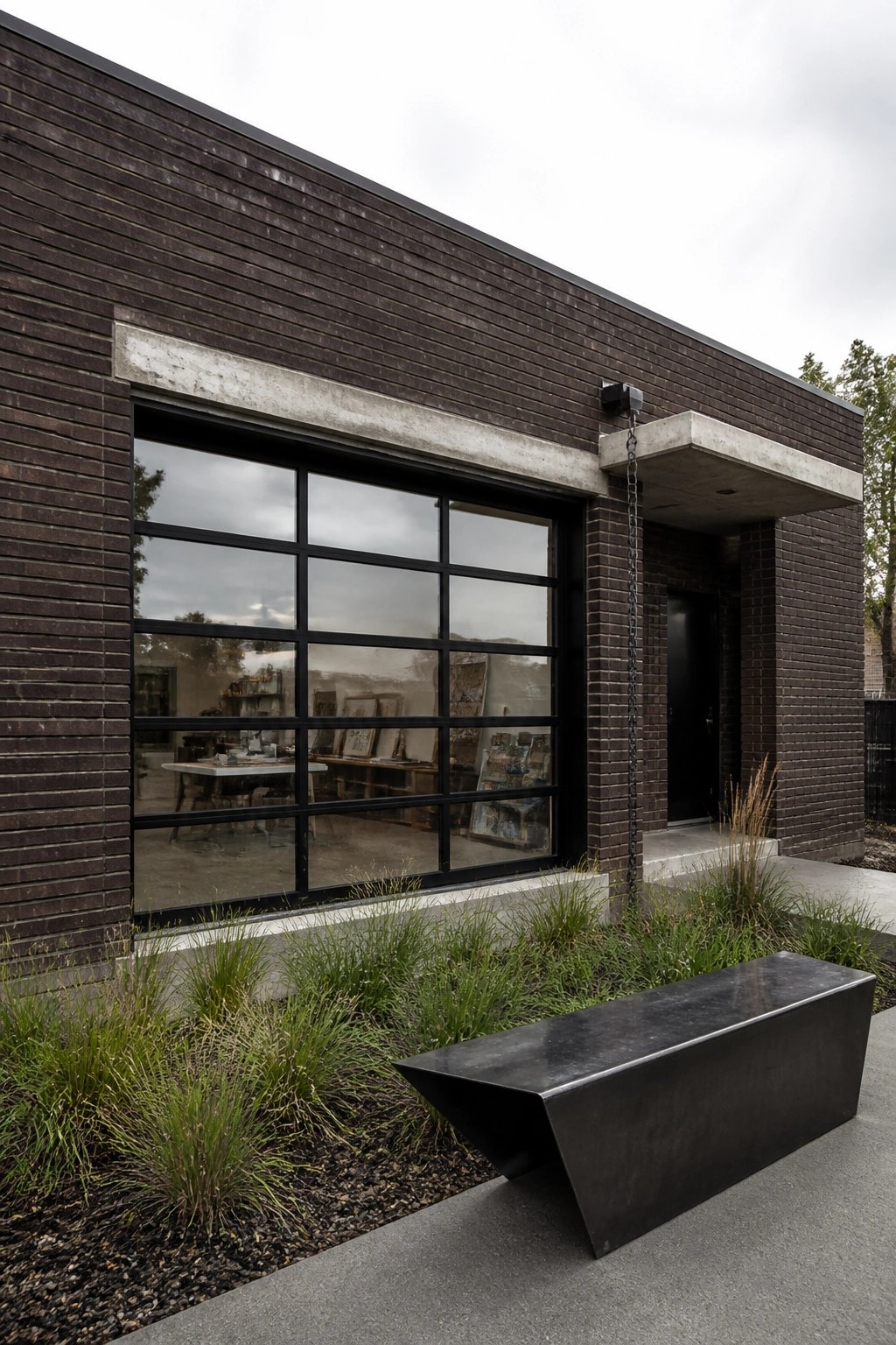 Modern dark brick building with large window, black bench, and front landscaping