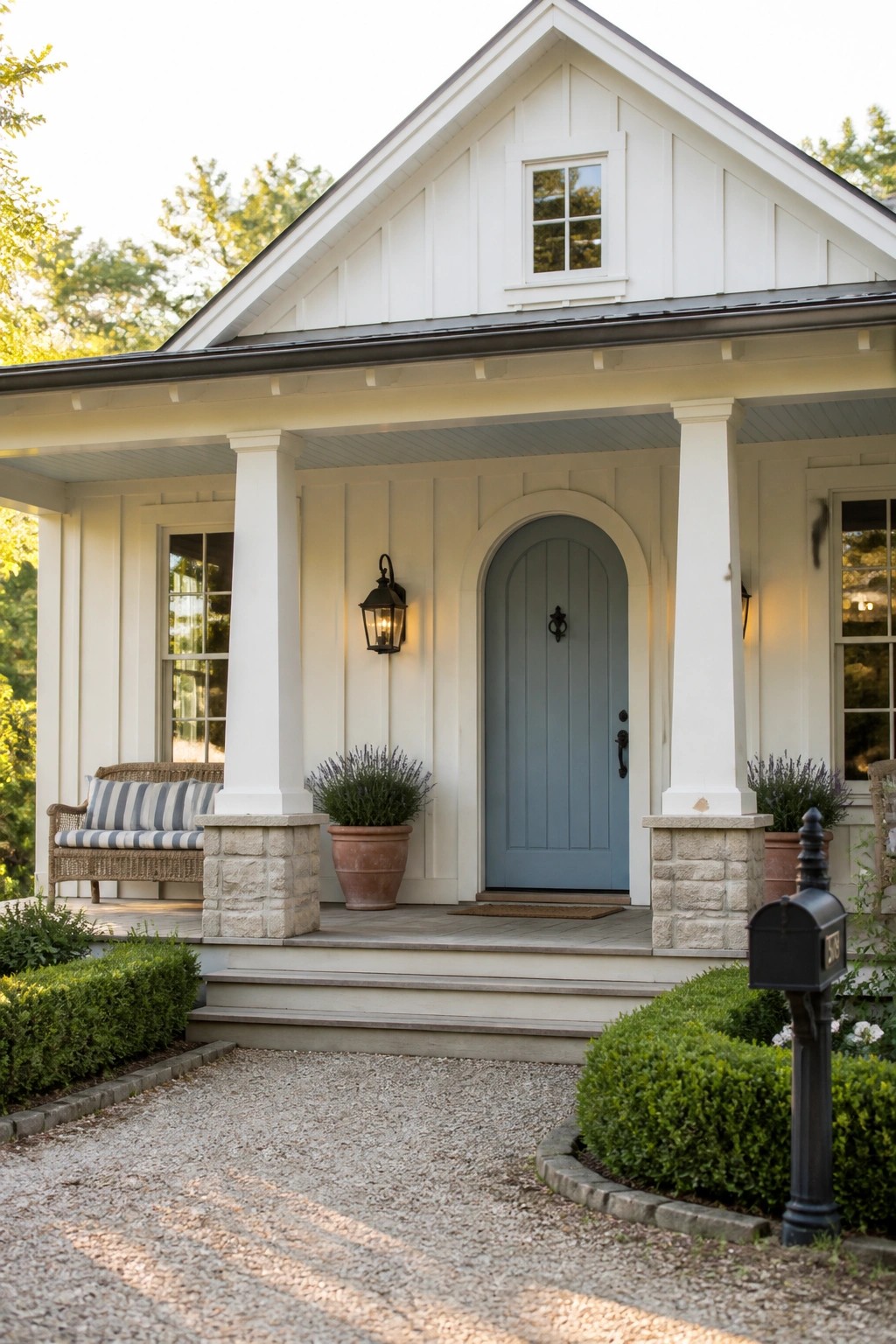 White house with blue arched door, stone porch columns, and black mailbox.