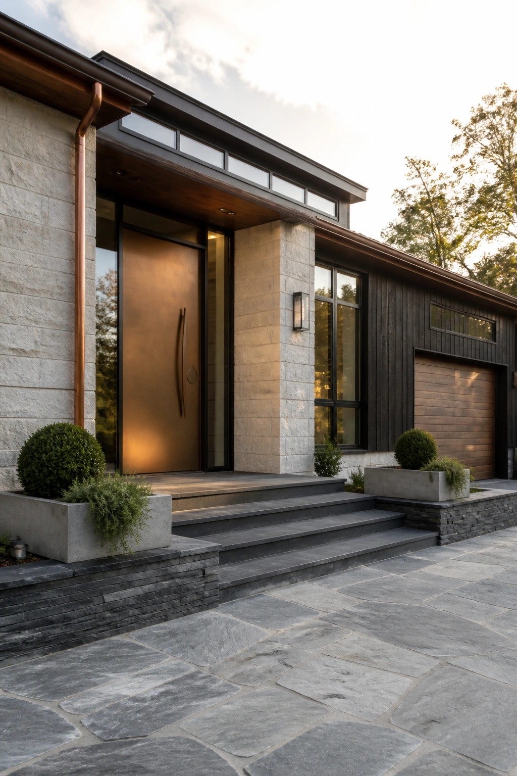 A modern house exterior featuring light stone walls, dark wood siding, a bronze front door, and wide stone steps.