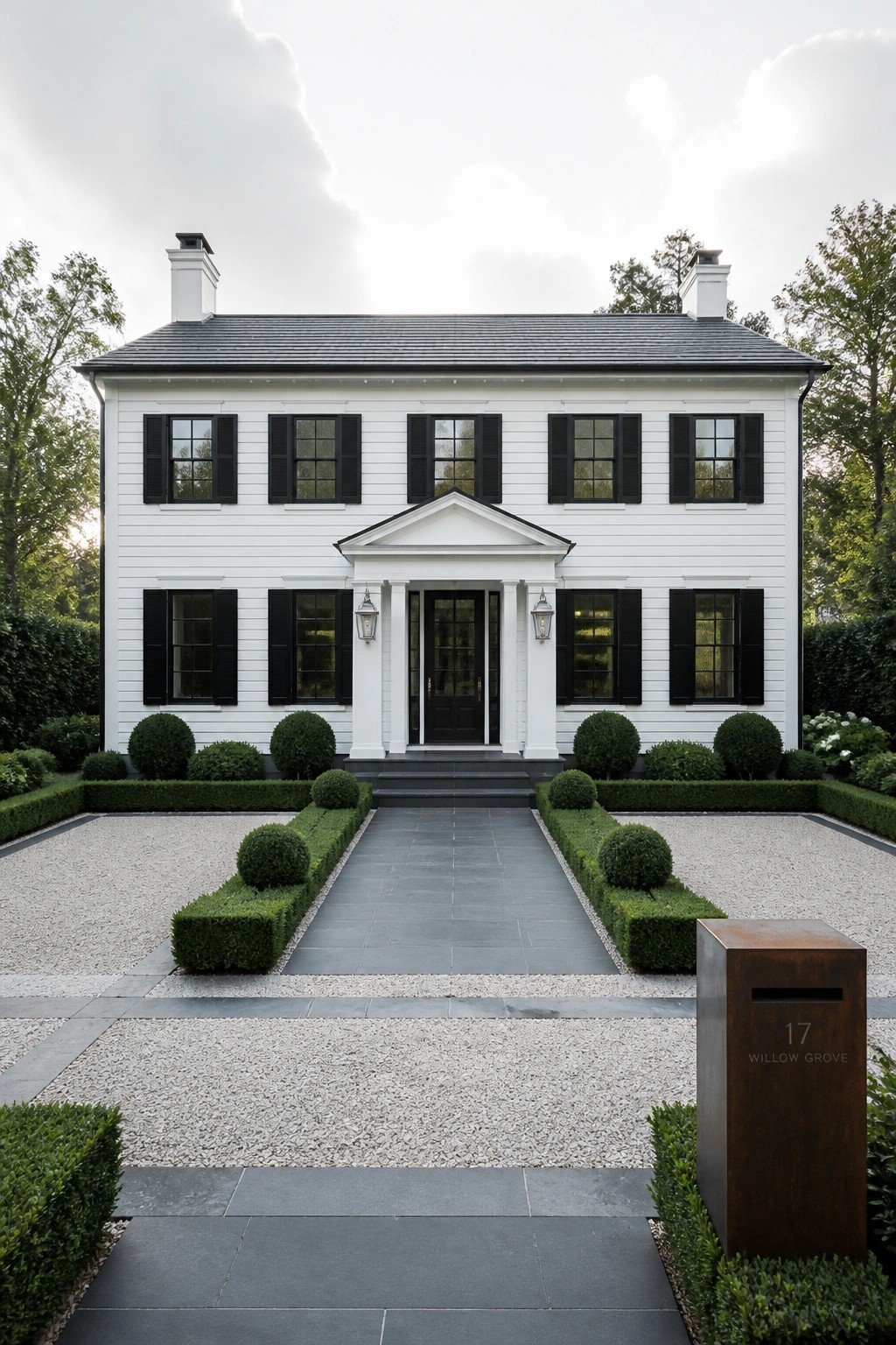 A two-story white house with black shutters on all windows, a central black door with white columns, and a formal front garden with boxwood hedges and gravel driveway.