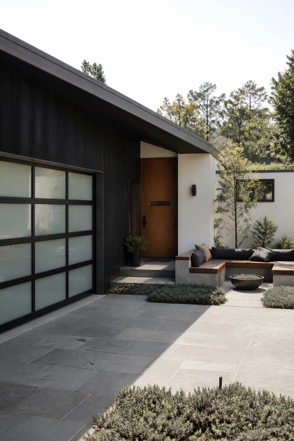 Modern dark wood home with wooden door, glass garage, and stone patio with seating.