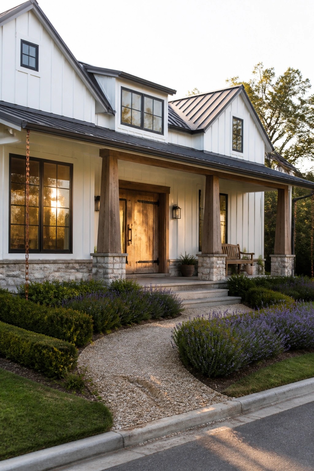 Front view of a white modern farmhouse with a covered porch, wooden columns resting on stone bases, double wood doors, and a gravel walkway.