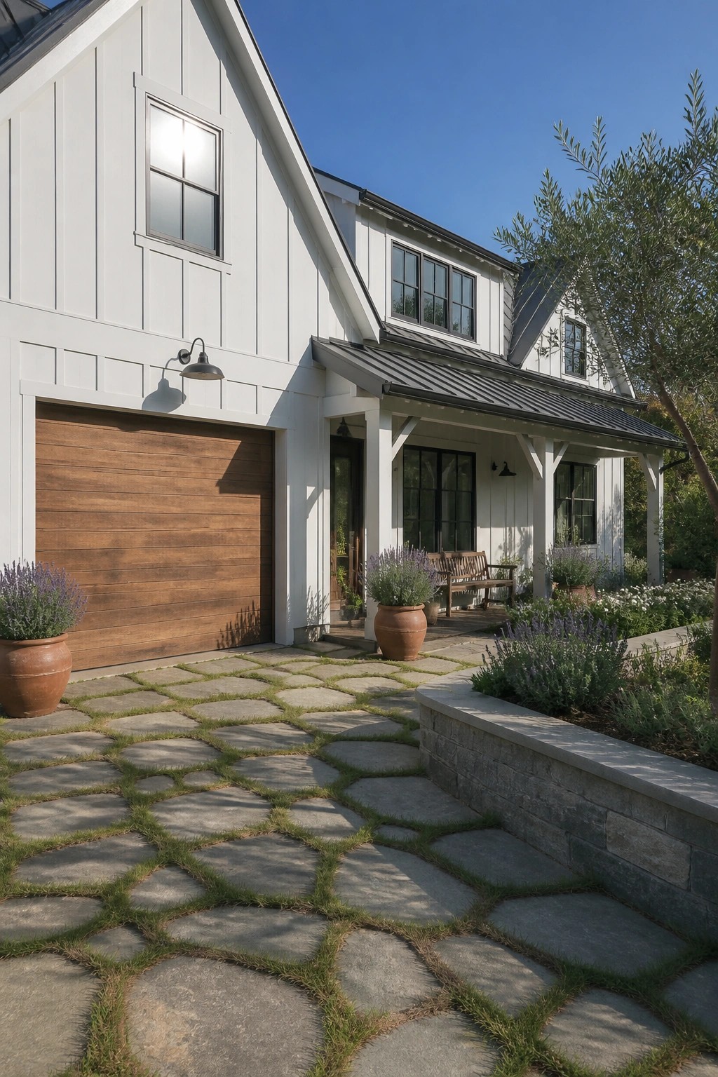 White farmhouse with wooden garage door, stone path, potted lavender, and sunny porch.