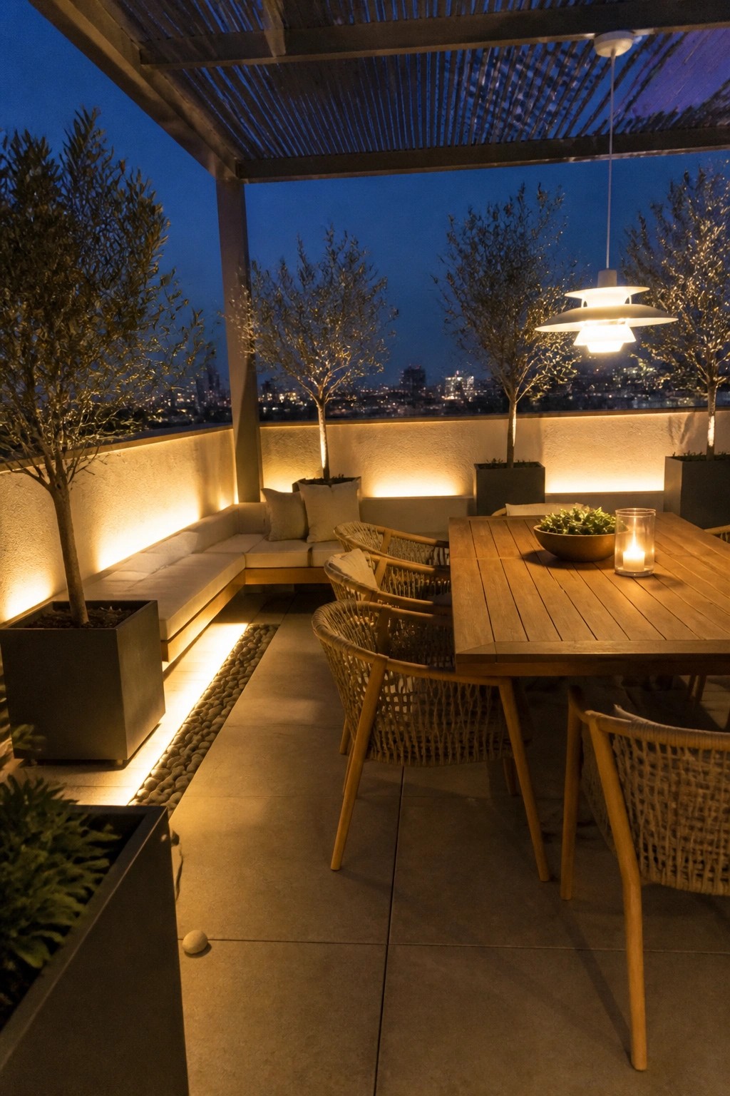 Modern rooftop terrace at night with wooden table, woven chairs, and illuminated trees