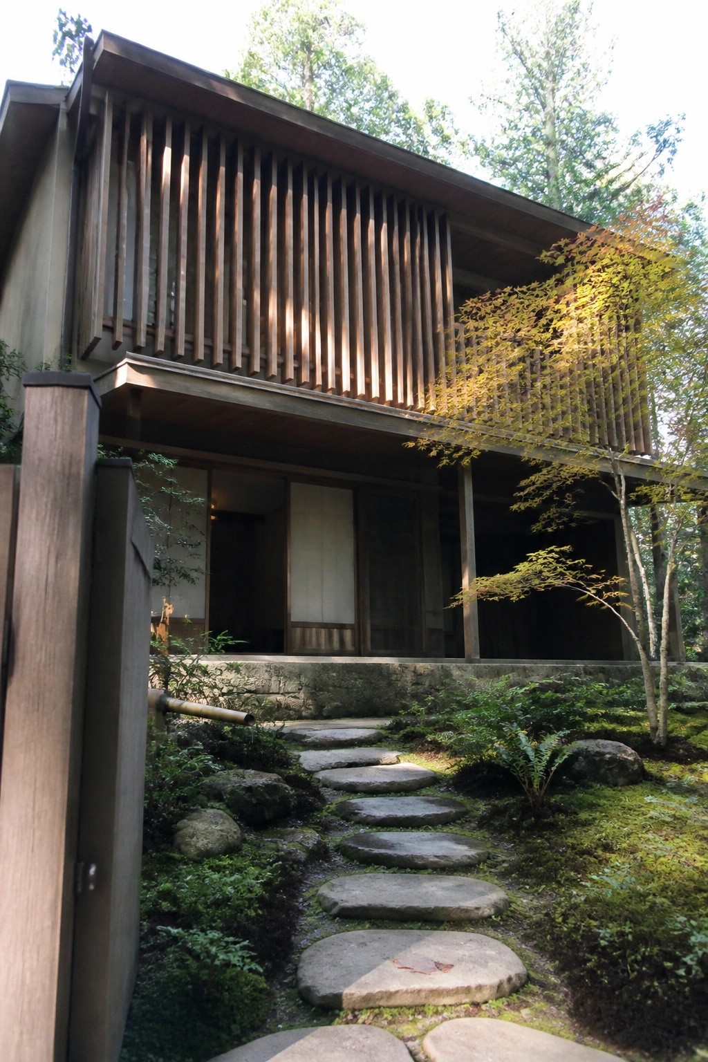 Traditional Japanese wooden house with stone path through mossy garden and trees